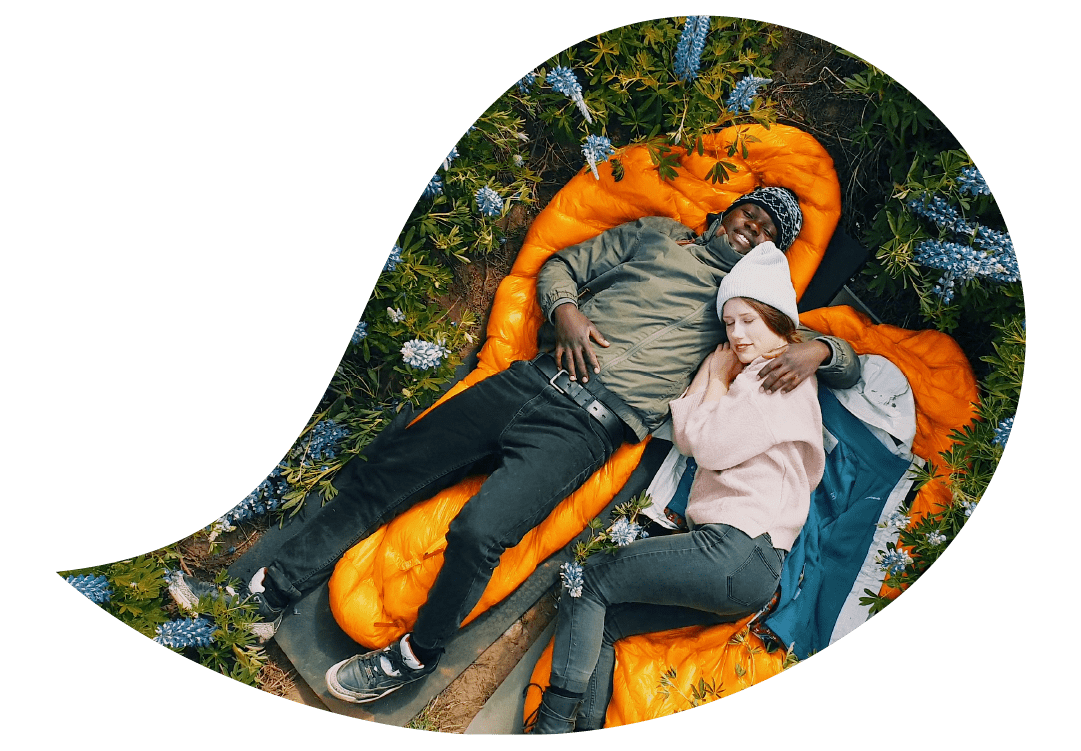 Mies ja nainen makaamassa makuupussien päällä niityllä